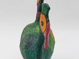 a green bird with a red beak on a white surface