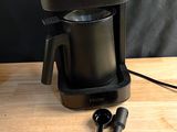 une cafetière noire posée sur une table en bois, avec une tasse noire
