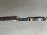 a black leather belt with two brass buckles on a gray surface