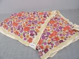 an orange and purple flowered blanket on a bed with a white pillow
