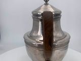 an antique silver plated teapot with wooden handle on a white table