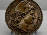 une vieille médaille en bronze représentant le visage d'une femme coiffée d'un chapeau