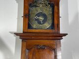 a wooden grandfather clock on a stand against a white wall