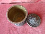 a small metal bowl with a lid on a pink cloth
