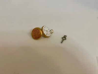 une petite horloge et une clé posées sur une surface blanche