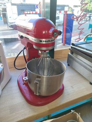 un robot de cuisine rouge posé sur un plan de travail, à côté d'une boîte de beignets