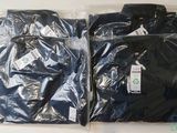 deux t-shirts noirs emballés dans du plastique, posés sur une table