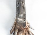 a wooden mask hanging on the wall with feathers on it