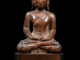 une statue en bois représentant un Bouddha assis sur une surface noire