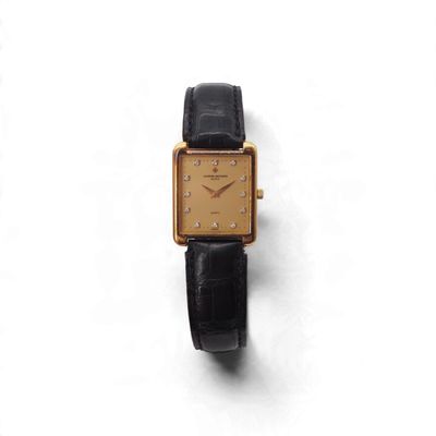 une montre en or avec un bracelet noir posée sur une surface blanche