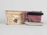une petite boîte recouverte d'un tissu, posée à côté d'un petit fer à repasser