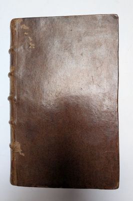 un vieux livre brun posé sur une table à côté d'un mur blanc