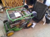 a green lawn mower sitting on the floor next to a trash can