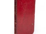 an old red book sitting on top of a white surface