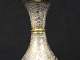 silver and gold vase sitting on a black surface with a black background
