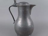 an old silver pitcher with a bird on the handle