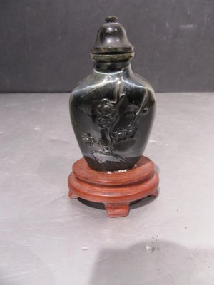 a small black vase on a wooden stand on a table