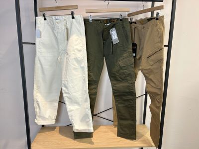 trois pantalons pour homme suspendus à un portant dans un magasin de vêtements