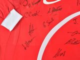 the shirt is red and white with a lot of autographs on it