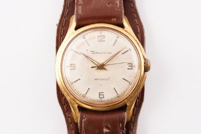 une montre en or avec un bracelet en cuir marron sur un fond blanc