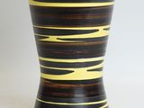yellow and black striped vase sitting on a white surface