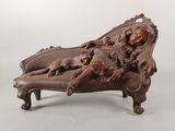 une photo d'une sculpture en bois représentant une femme et un chien allongés sur une chaise longue