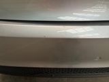 the front bumper of a silver car with a dent on it