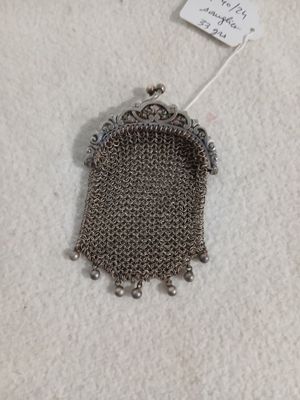 un petit porte-monnaie en métal muni d'une chaîne, posé sur une surface blanche