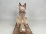 statue of a cat sitting on top of a wooden block on a white surface