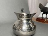 a silver pitcher sitting on a table next to a black bird