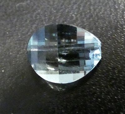 an image of a faceted blue topazte stone on a black surface