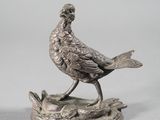 a silver statue of a bird sitting on a tree stump