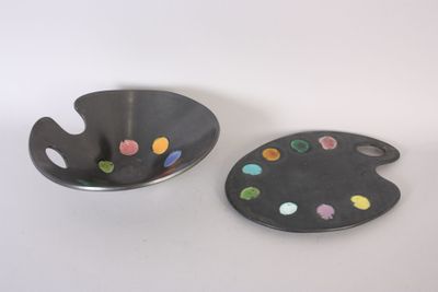 deux assiettes contenant de la peinture et une palette, posées sur une surface blanche