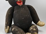 un ours en peluche noir assis par terre, avec une langue rouge