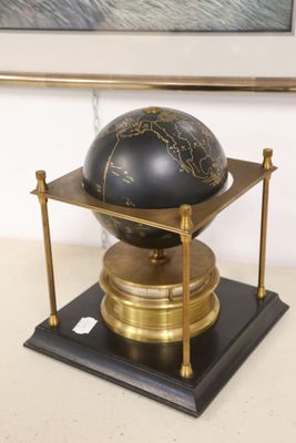 a black and gold globe on a stand with a painting in the background