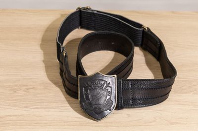 une ceinture noire munie d'une boucle métallique posée sur une table en bois