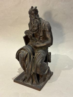 bronze statue of a man sitting on a chair with a book in his lap
