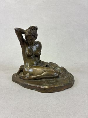 bronze statue of a woman sitting on a rock with her hands behind her head