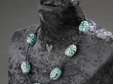 Collier de perles vertes et blanches sur un mannequin devant un fond noir