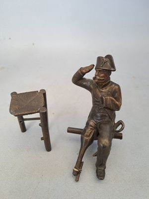 a bronze statue of a man sitting on a bench next to a chair