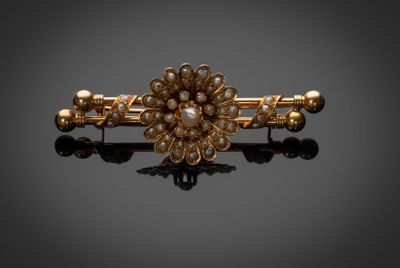 un gros plan sur une broche en forme de fleur, en or et perles