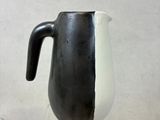 a black and white pitcher sitting on a clear stand