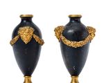 pair of black and gold vases on marble bases on a white background