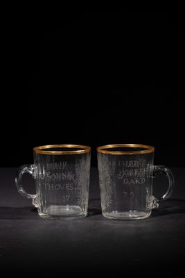 two clear glass cups with gold rims on a black surface