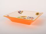 an orange bowl with flowers on it on a white surface