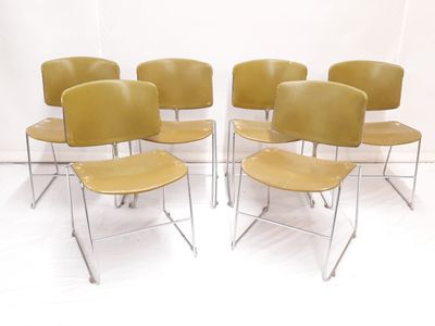 six chaises jaunes empilées les unes sur les autres dans une pièce blanche