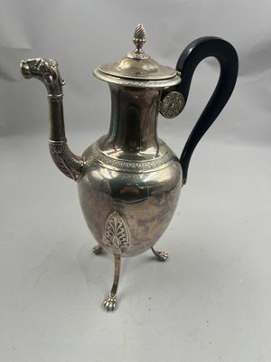 une théière ancienne en argent, avec une anse noire, posée sur un socle