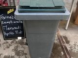 a green trash can sitting on the floor in front of a table