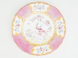 une assiette rose et jaune ornée d'un oiseau, posée sur un fond blanc