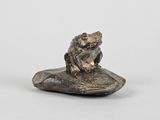 une image représentant une grenouille assise sur un rocher posé sur une surface blanche